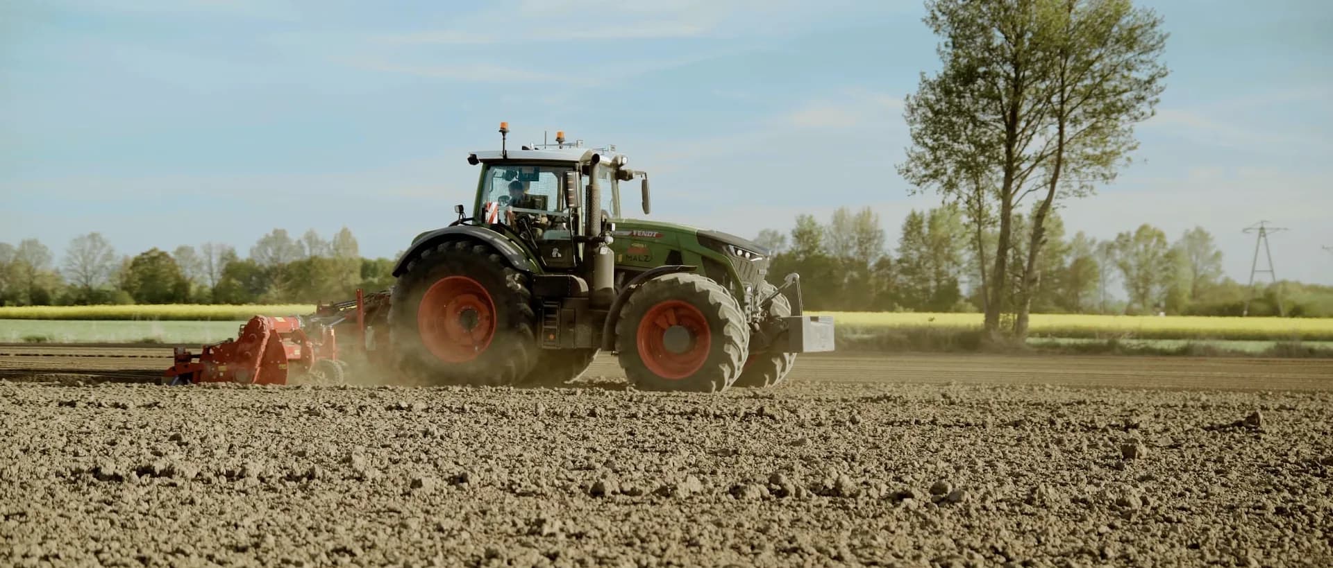 Ciągnik Fendt z agregatem uprawowym przygotowuje pole, w tle kwitnący rzepak